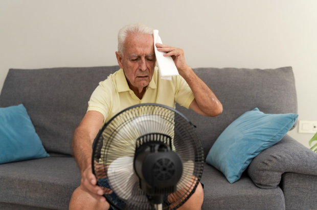 Elderly man cooling off in front of a fan inside his home.