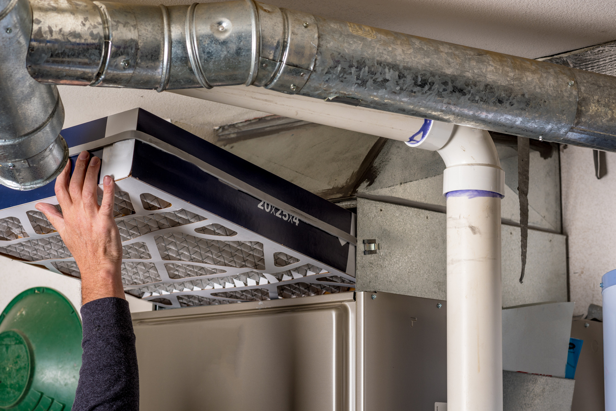 A person is replacing an HVAC filter, holding a new filter near the air duct system.